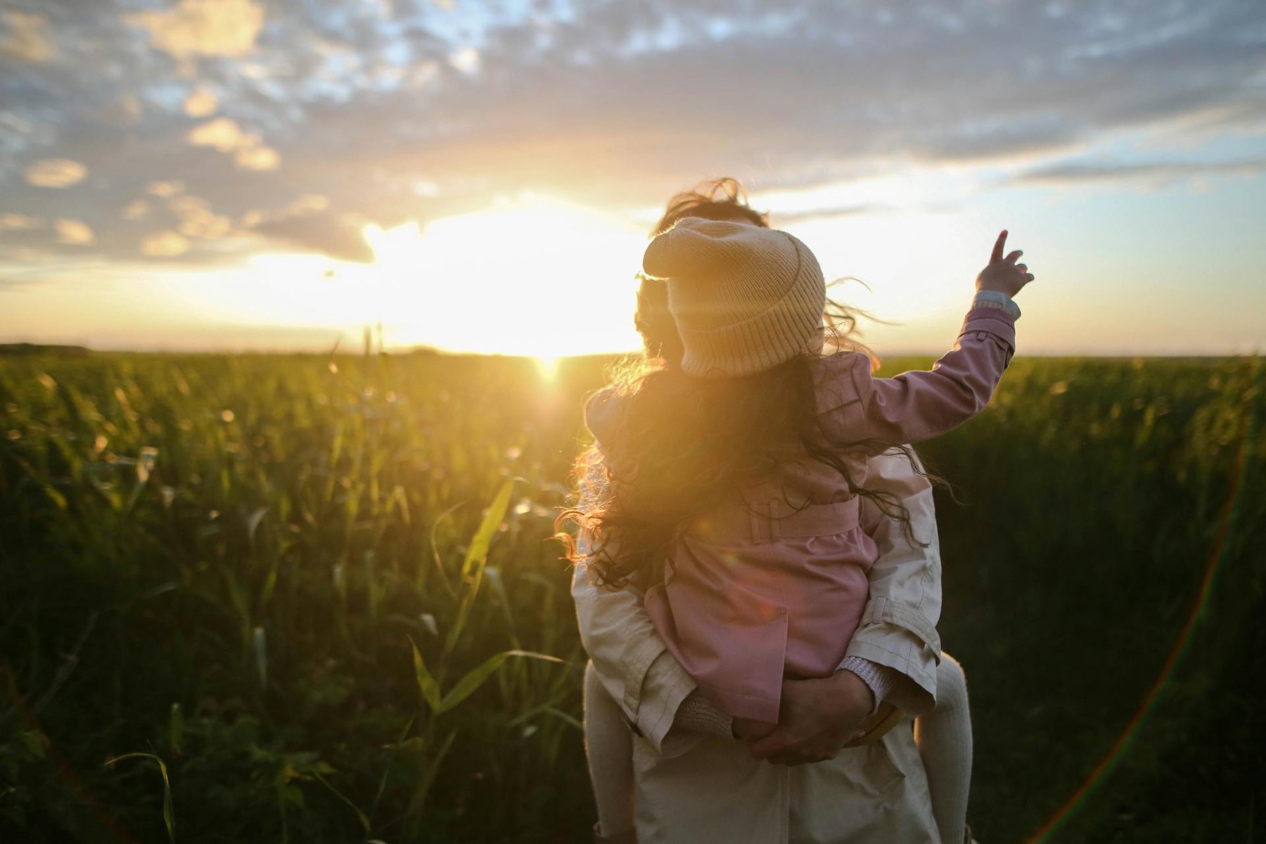 A parent carrying their young daughter on their shoulders through a field at sunset